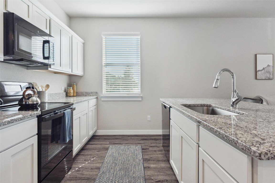 523 Powell Drive, Unit 1101 Leander, TX 78641 - Photo 9 of 24 Kitchen with black appliances, white cabinets, dark wood-style floors, and light stone countertops