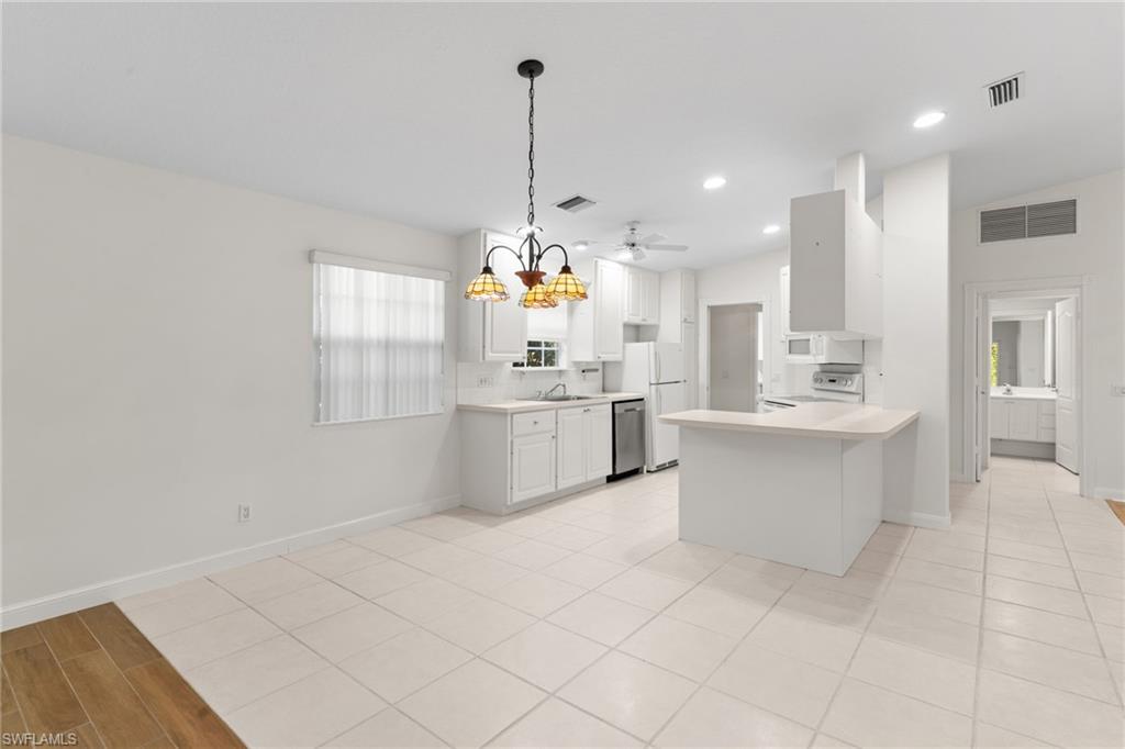 4907 Kingston Way Naples, FL 34119 - Photo 13 of 49 a large white kitchen with kitchen island a stove a sink dishwasher and white cabinets with wooden floor