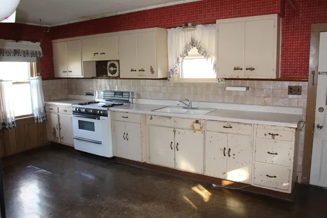 a kitchen with white cabinets a sink a stove and wooden floors