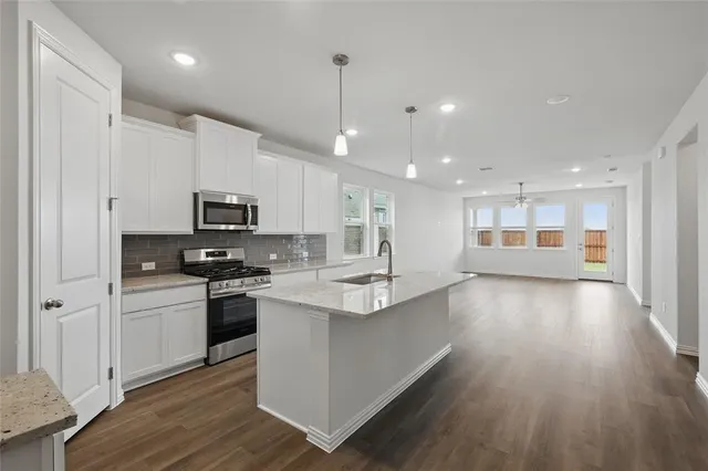 a kitchen with stainless steel appliances kitchen island granite countertop a stove top oven a sink dishwasher and a refrigerator with wooden floor