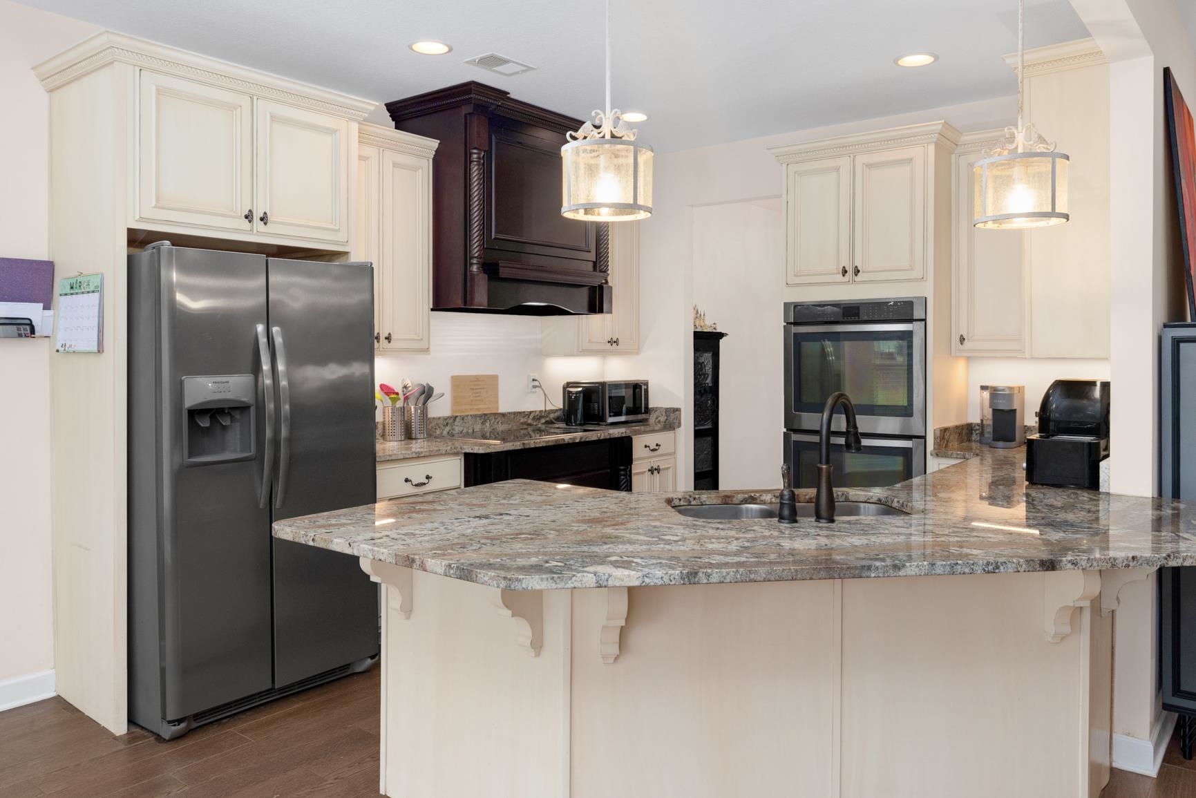 504 Bankston Road Nesbit, MS 38651 - Photo 15 of 39 Modern kitchen featuring an angled island with a built-in sink and dark faucet, cream cabinetry, a stainless steel side-by-side refrigerator, double wall ovens, and pendant lighting