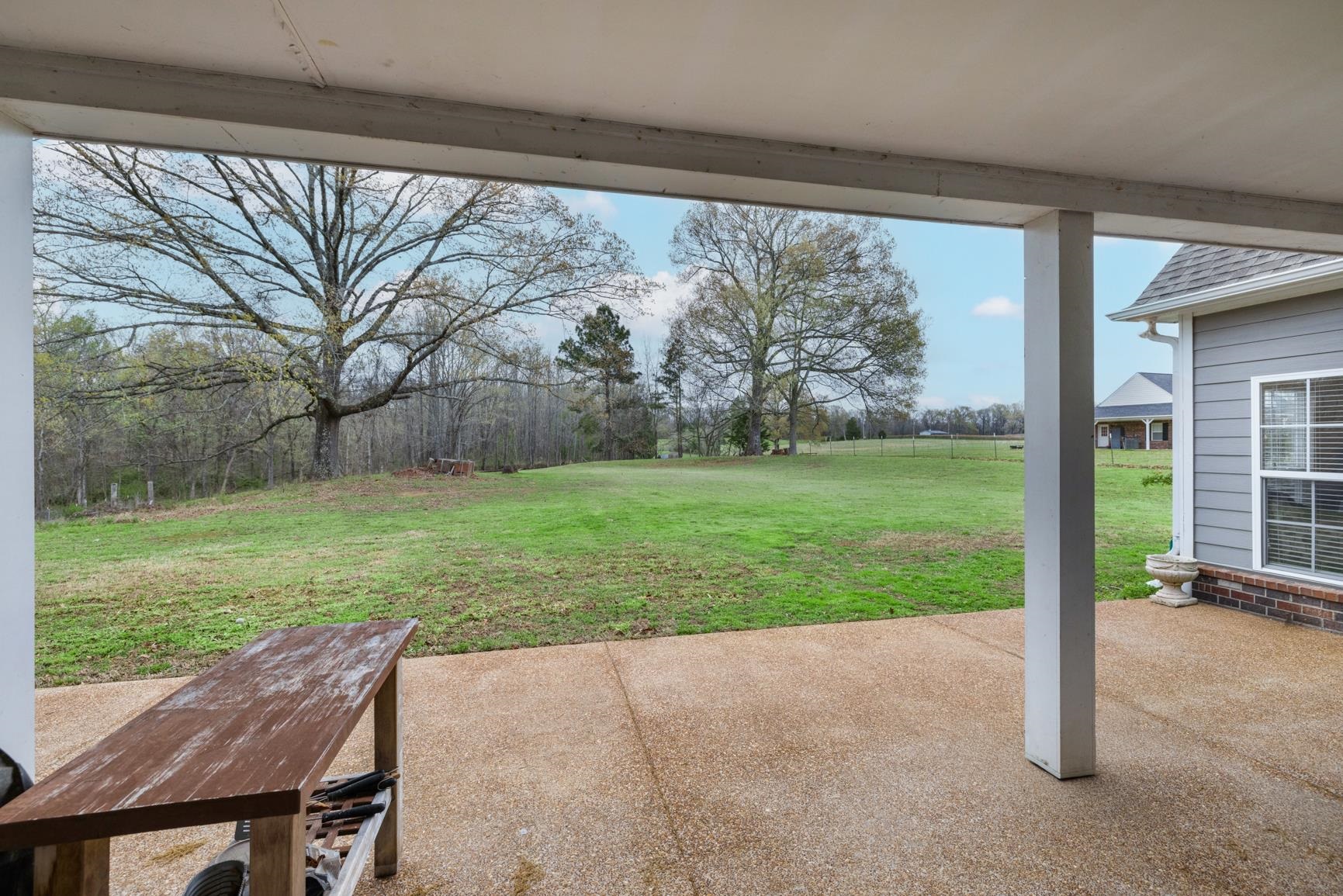 504 Bankston Road Nesbit, MS 38651 - Photo 29 of 39 Expansive covered patio featuring a textured concrete surface, white support columns, and views of a large grassy field with mature trees