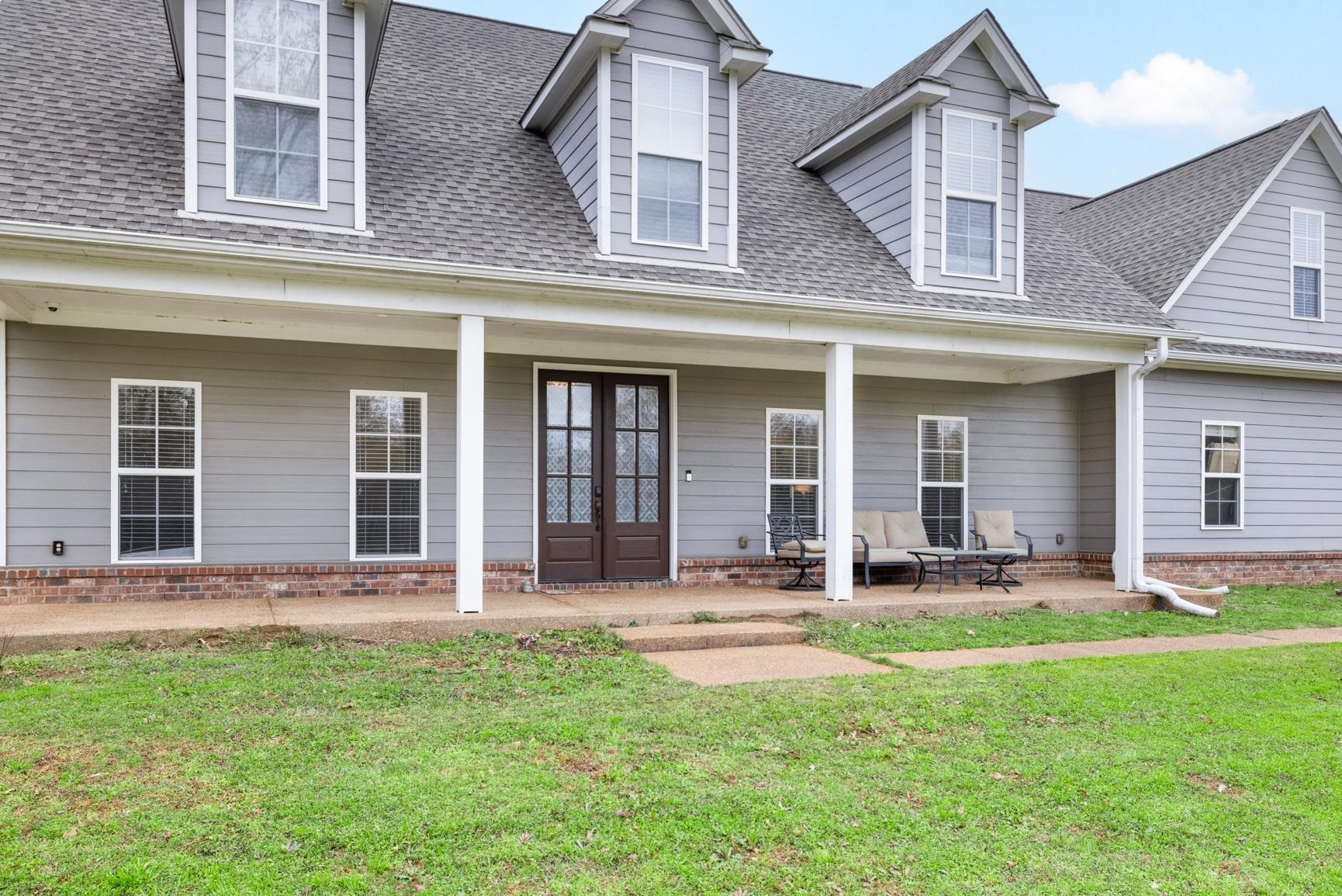 504 Bankston Road Nesbit, MS 38651 - Photo 3 of 39 Exterior facade featuring light gray siding, white trim, a covered porch, dark double entry doors with decorative glass, and multiple gabled dormers