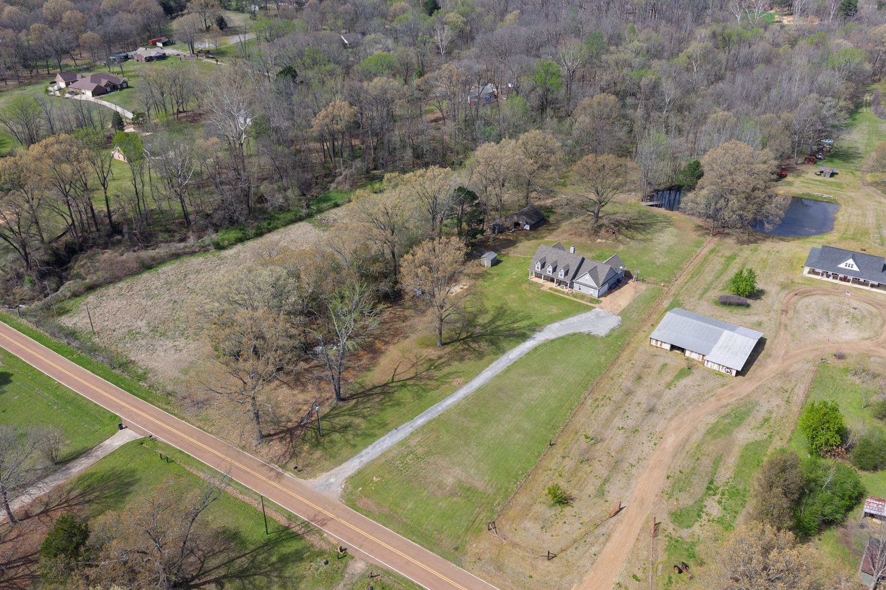 504 Bankston Road Nesbit, MS 38651 - Photo 34 of 39 Expansive rural property featuring a main residence with a gray exterior and multiple gables, a long gravel driveway, a large barn structure with a metal roof, and a visible pond