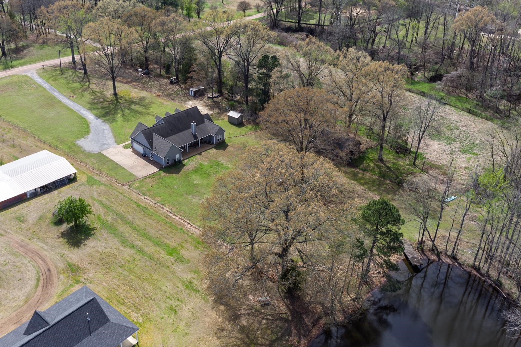 504 Bankston Road Nesbit, MS 38651 - Photo 36 of 39 Spacious property featuring a single-story residence with an attached garage, a large detached outbuilding, and a pond with a pier