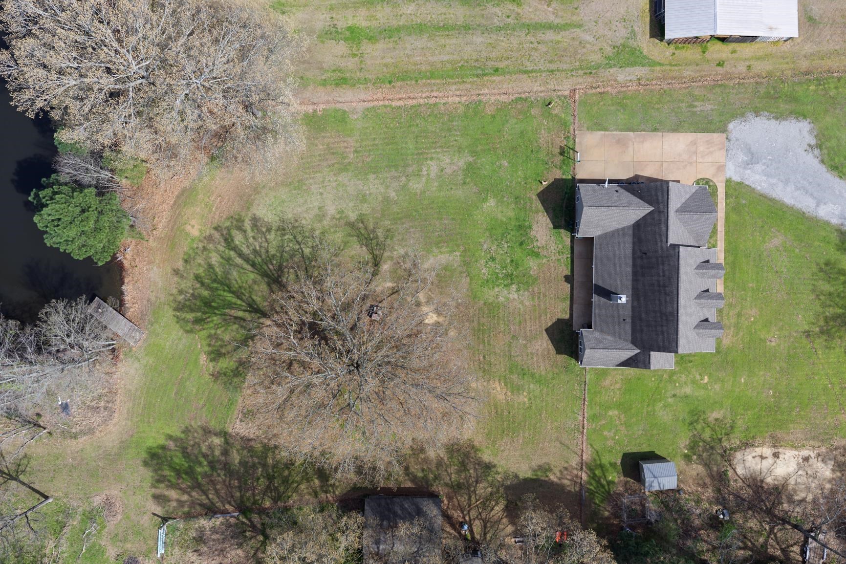 504 Bankston Road Nesbit, MS 38651 - Photo 37 of 39 Expansive property featuring a private pond with a wooden dock, mature trees, a main residence with a multi-gabled roof, a paved driveway, and a detached shed