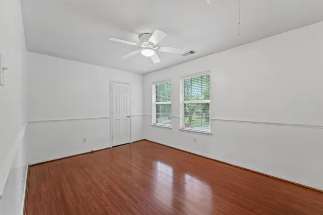 an empty room with wooden floor fan and windows