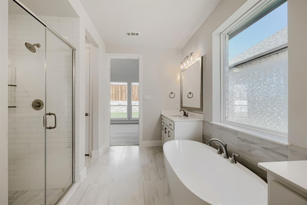 4407 Windy Point Road Oak Point, TX 75068 - Photo 21 of 27 Contemporary bathroom featuring a freestanding soaking tub, glass-enclosed shower, dual vanity with quartz countertop, and large window with privacy film