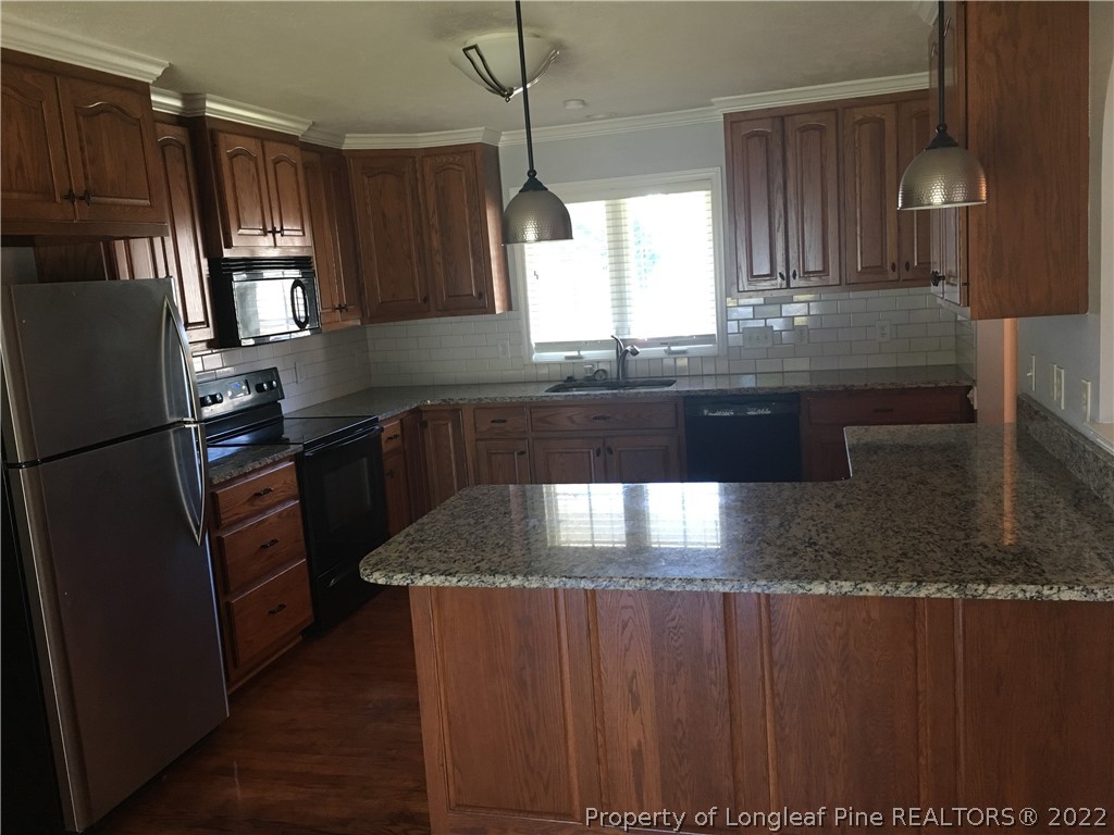 1409 Blue Ribbon Lane Hope Mills, NC 28348 - Photo 5 of 19 a kitchen with granite countertop a refrigerator a sink and wooden cabinets