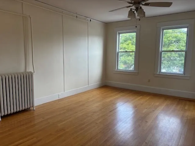 an empty room with wooden floor chandelier fan and windows