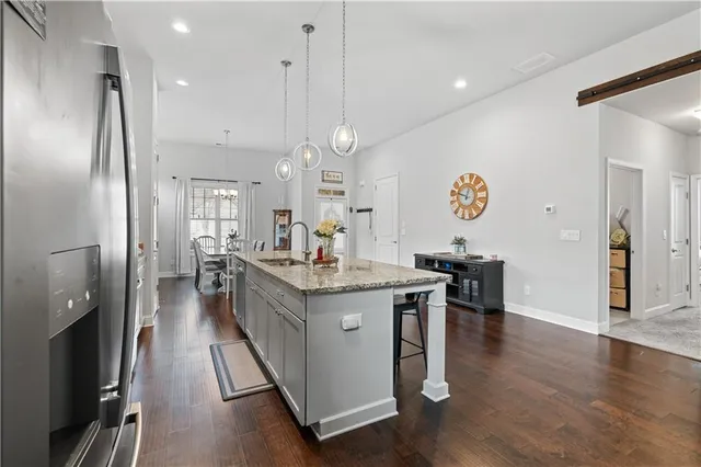 a kitchen with stainless steel appliances granite countertop a refrigerator a sink dishwasher a oven and a dining table with wooden floor