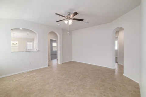 an empty room with chandelier fan and windows