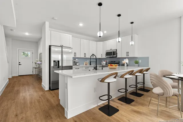 a kitchen with stainless steel appliances kitchen island granite countertop a refrigerator a stove top oven a sink dishwasher and a dining table with wooden floor