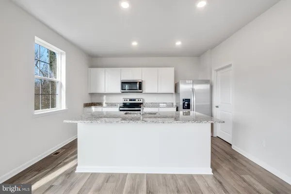 a large kitchen with stainless steel appliances granite countertop a stove a sink a refrigerator and white cabinets with wooden floor