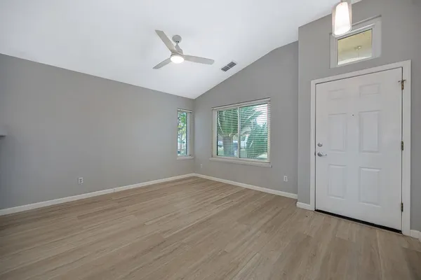 an empty room with wooden floor fan and windows