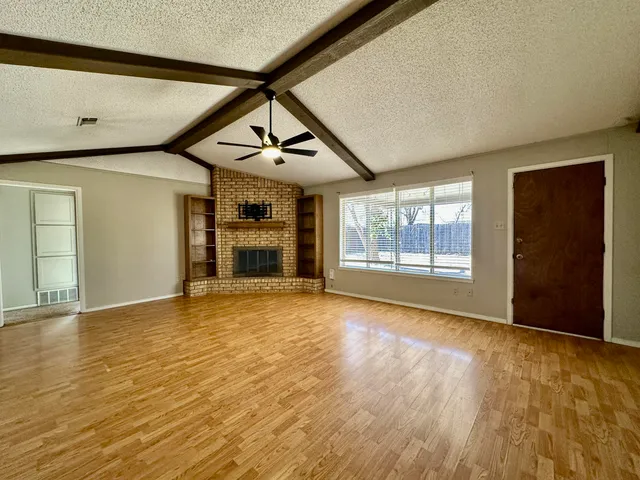 a view of an empty room with a window and wooden floor