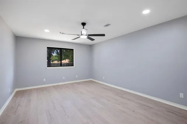 a view of an empty room with wooden floor and a ceiling fan