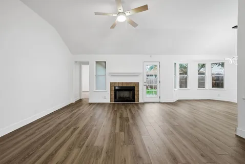 a view of an empty room with wooden floor fireplace and a window