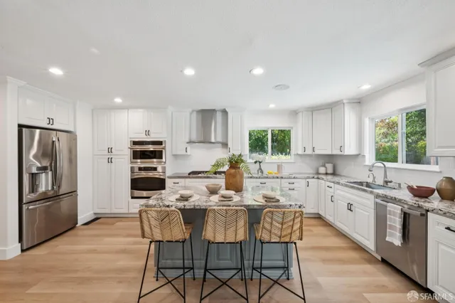 a kitchen with stainless steel appliances granite countertop a stove a sink a refrigerator with white cabinets and wooden floor