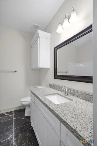 a bathroom with a granite countertop sink a toilet and a mirror