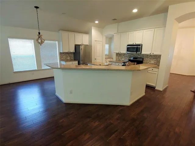 a kitchen with stainless steel appliances granite countertop a sink a microwave a refrigerator a stove a microwave and wooden floors