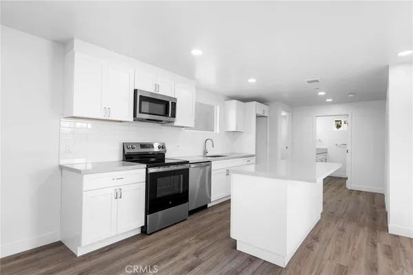 a kitchen with stainless steel appliances granite countertop a stove top oven a sink a refrigerator and white cabinets with wooden floor