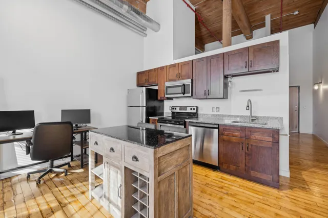 a kitchen with stainless steel appliances granite countertop a stove top oven a sink dishwasher and a refrigerator with wooden cabinets