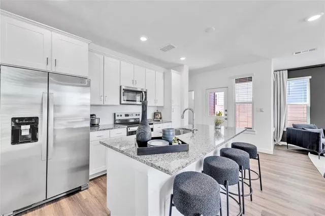 a kitchen with stainless steel appliances granite countertop a refrigerator a sink a stove a dining table and chairs with wooden floor