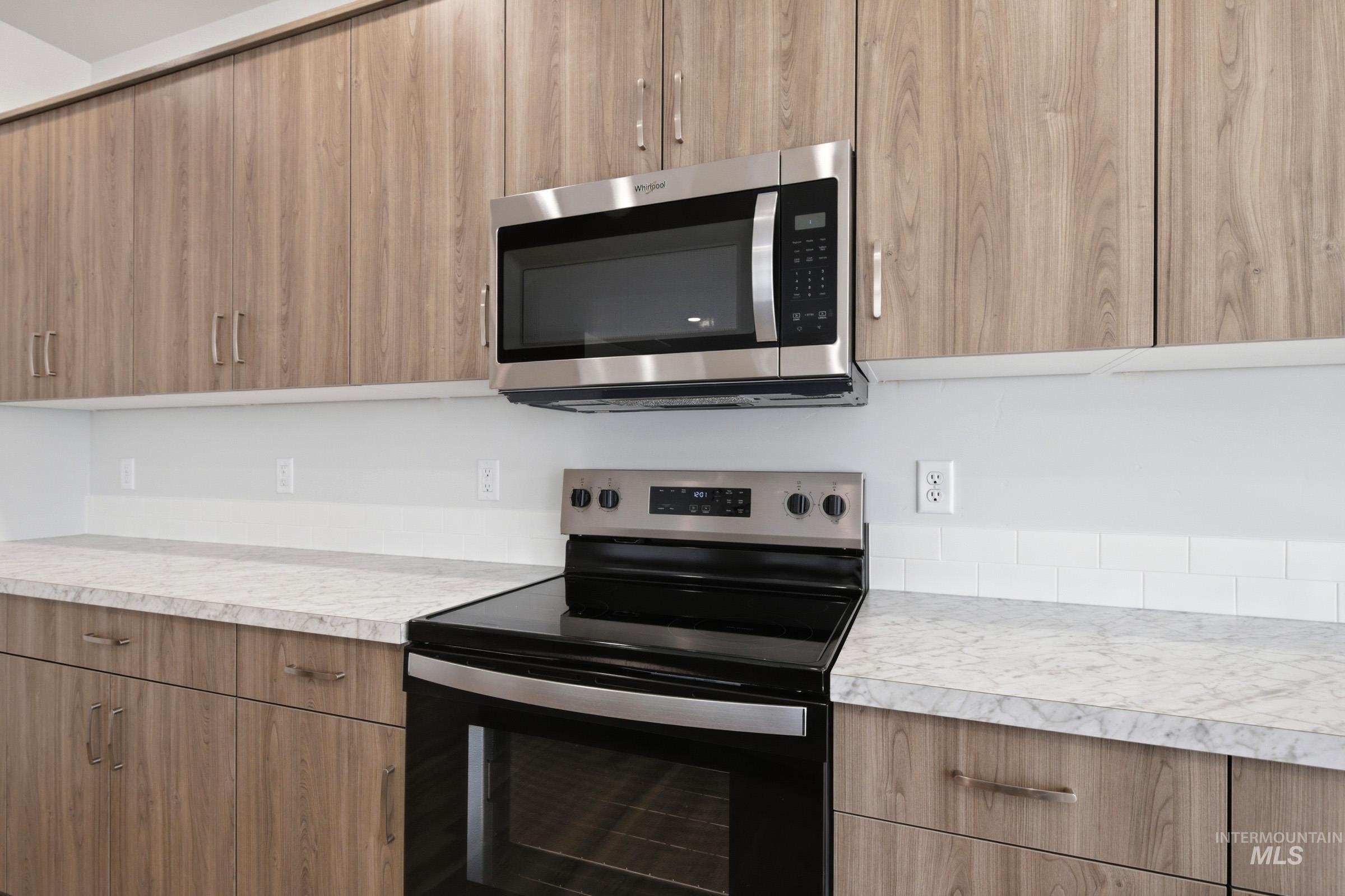 13649 Inman Court Caldwell, ID 83607 - Photo 8 of 22 Kitchen featuring wood-finish cabinetry with stainless steel hardware, a stainless steel over-the-range microwave, a black electric range with stainless steel accents, white subway tile backsplash, and light-toned countertops