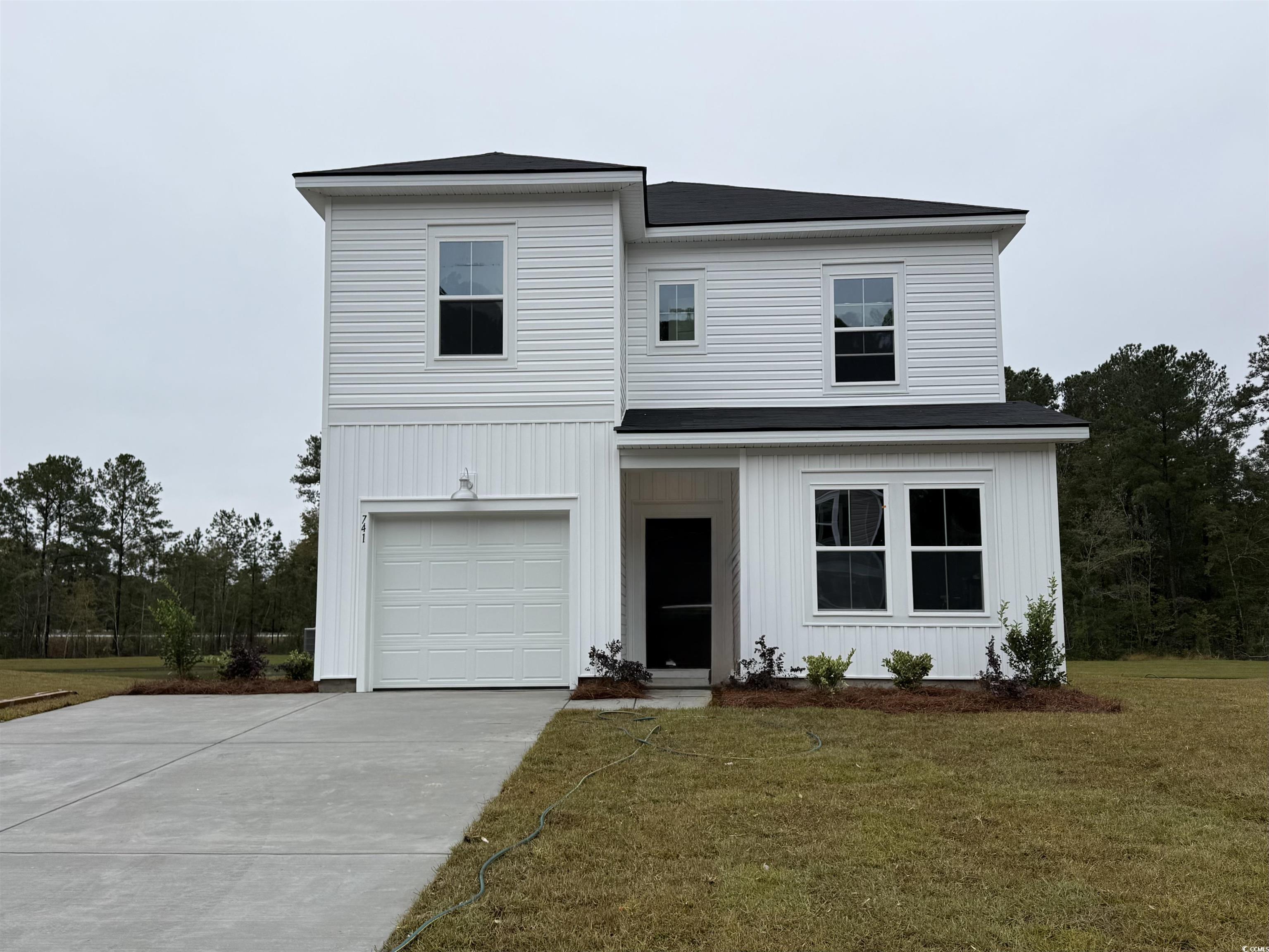 View of front facade featuring a front yard, a garage, concrete driveway, and board and batten siding