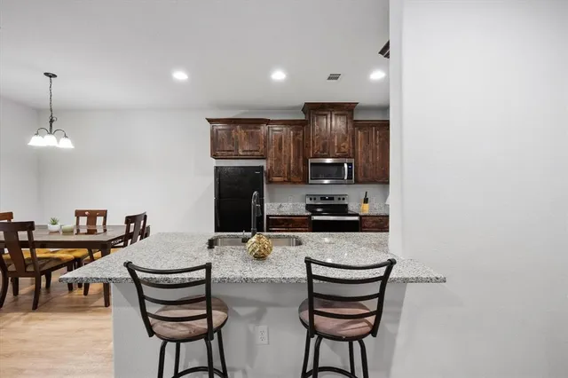 a kitchen with stainless steel appliances kitchen island granite countertop a stove a sink a dining table and chairs with wooden floor