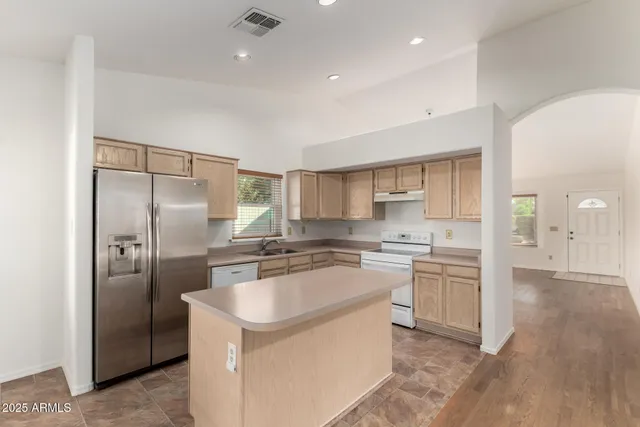 a kitchen with stainless steel appliances granite countertop a refrigerator a sink a stove and white cabinets with wooden floor