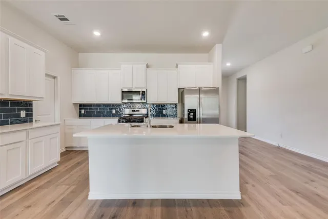 a view of kitchen with stainless steel appliances granite countertop a stove top oven a sink dishwasher and a refrigerator with wooden floor