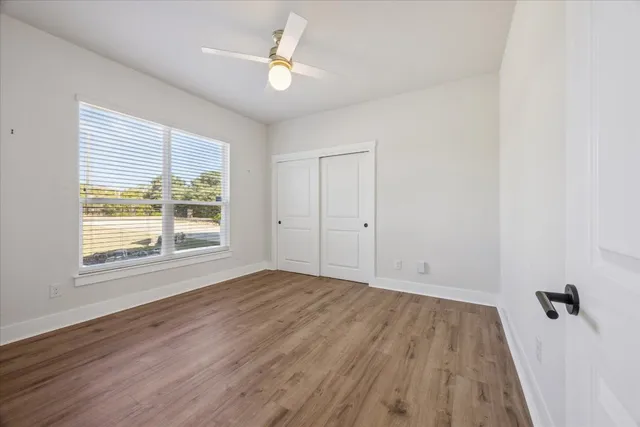 an empty room with wooden floor fan and windows
