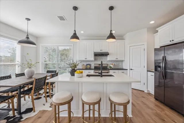 a kitchen with stainless steel appliances granite countertop a sink a stove a refrigerator and chairs