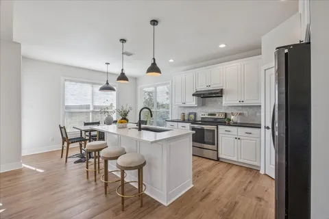 a kitchen with a sink a stove a refrigerator and white cabinets with wooden floor