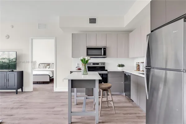 a kitchen with a refrigerator a stove a microwave oven a sink and chairs with wooden floor