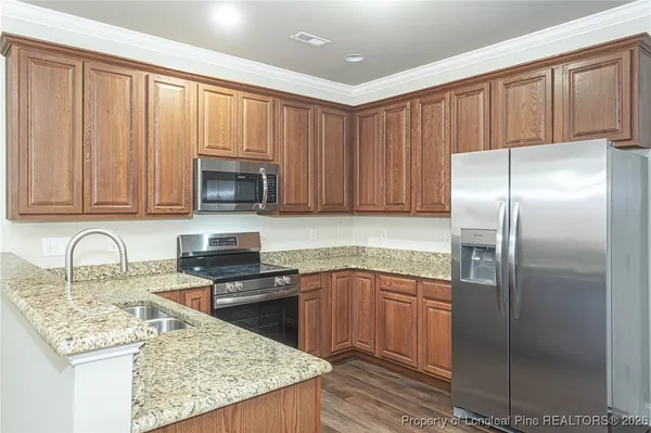 a kitchen with stainless steel appliances granite countertop a refrigerator a stove and a sink with wooden cabinets