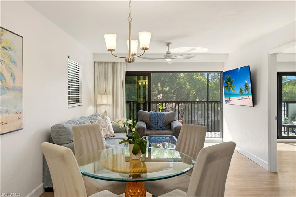 600 Neapolitan Way, Unit 254 Naples, FL 34103 - Photo 16 of 42 Dining room featuring ceiling fan, wood finished floors, a chandelier, and plenty of natural light