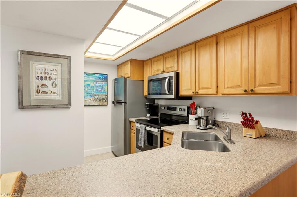 600 Neapolitan Way, Unit 254 Naples, FL 34103 - Photo 10 of 42 Kitchen featuring stainless steel appliances, light wood finish cabinetry, light stone countertops, and light tile patterned flooring