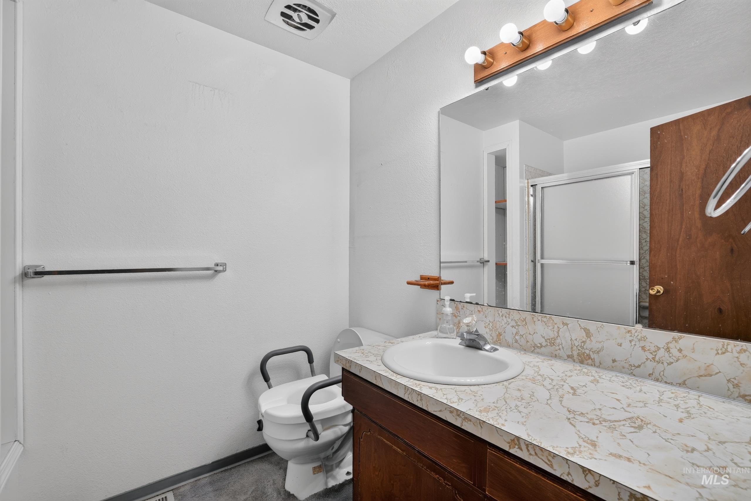 9055 West Highlander Road Boise, ID 83709 - Photo 26 of 39 Vanity with a built-in sink and stone-finish countertop, mirrored wall, and a shower with a sliding glass enclosure