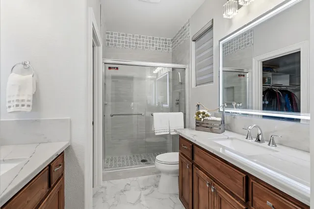 a bathroom with a granite countertop sink a toilet a mirror and shower