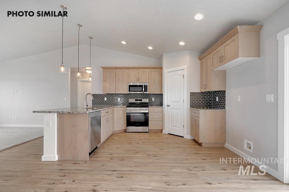 1676 Haystack Road Emmett, ID 83617 - Photo 8 of 32 Contemporary kitchen featuring light wood-finish cabinetry, stainless steel appliances, a dark subway tile backsplash, and a granite-topped island with a stainless steel sink and dishwasher