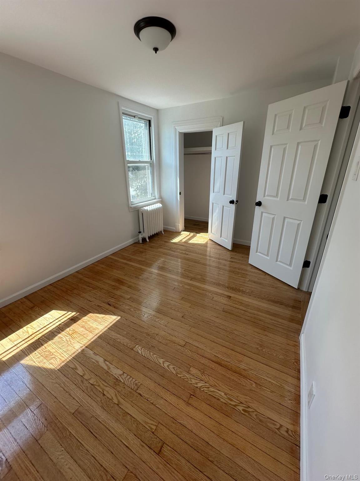 218-17 109th Avenue Queens, NY 11429 - Photo 18 of 35 Unfurnished bedroom featuring radiator heating unit, light wood-type flooring, and a closet