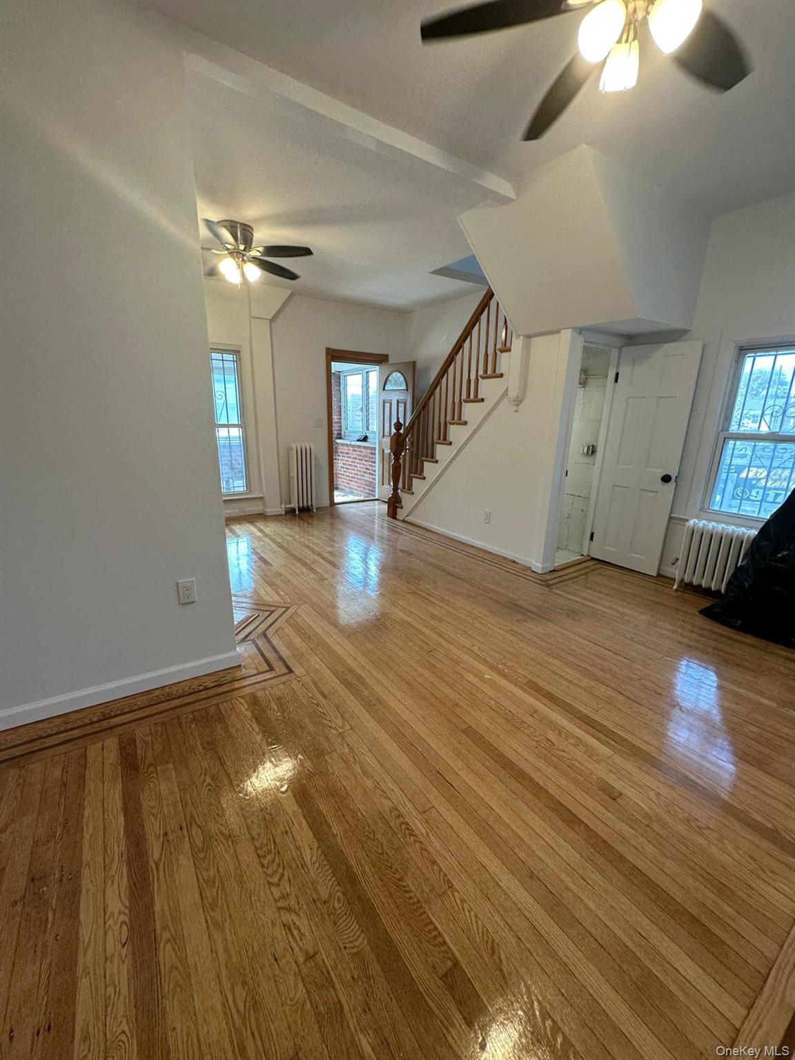 218-17 109th Avenue Queens, NY 11429 - Photo 32 of 35 Unfurnished living room featuring a ceiling fan, stairway, light wood-type flooring, radiator heating unit, and healthy amount of natural light