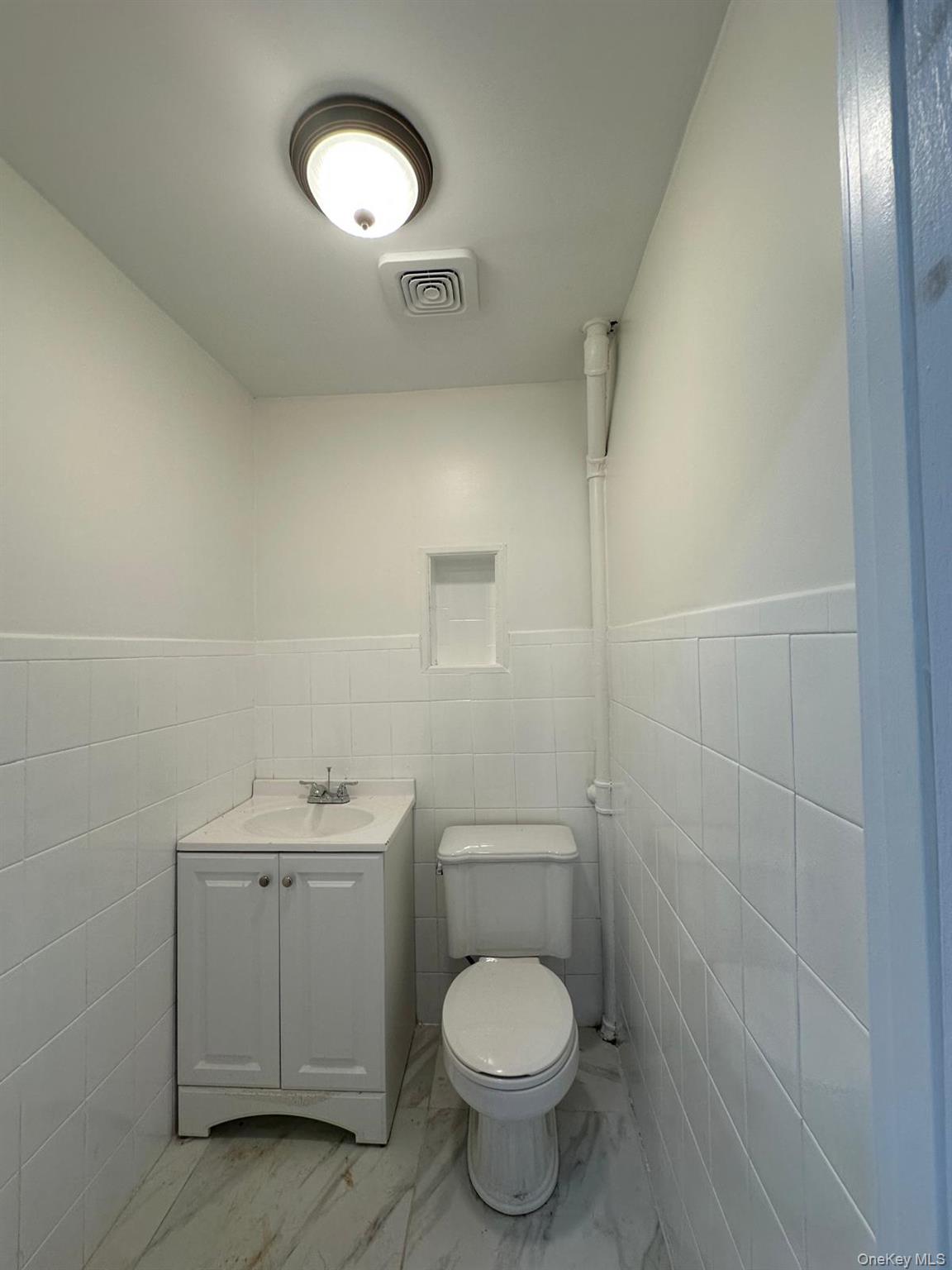 218-17 109th Avenue Queens, NY 11429 - Photo 35 of 35 Half bathroom featuring tile walls, vanity, a wainscoted wall, and light marble finish flooring