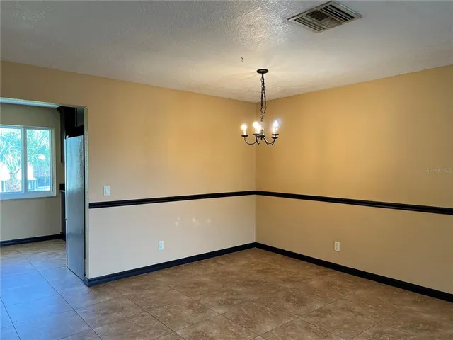 a view of an empty room with chandelier fan and a refrigerator