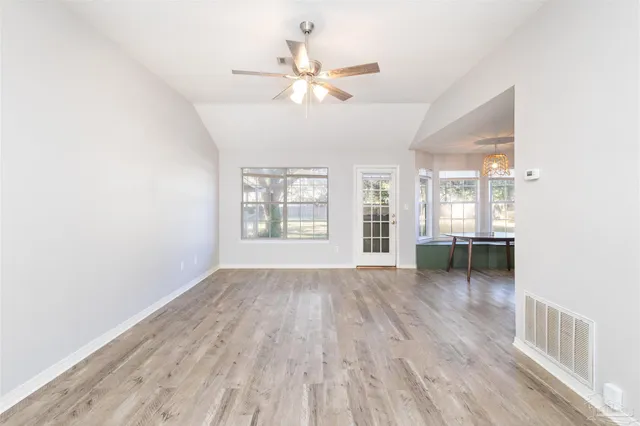 an empty room with wooden floor fan and windows