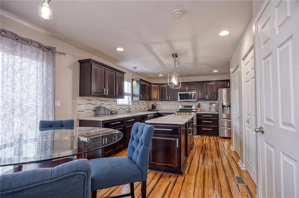 a kitchen with stainless steel appliances granite countertop a stove top oven a sink dishwasher a dining table and chairs with wooden floor