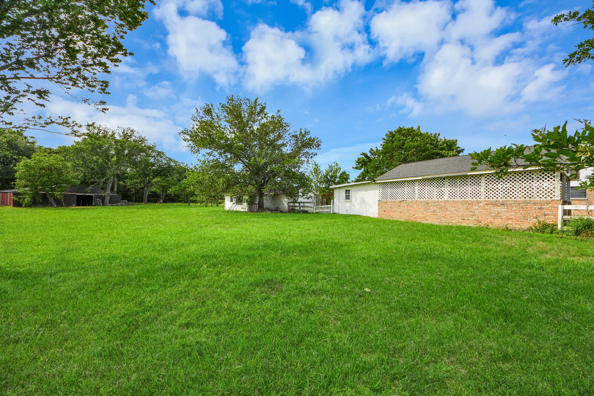 12746 Roy Road Pearland, TX 77581 - Photo 39 of 47 Spacious backyard with lush green grass, mature trees, and a partially brick exterior building, perfect for outdoor activities and relaxation.